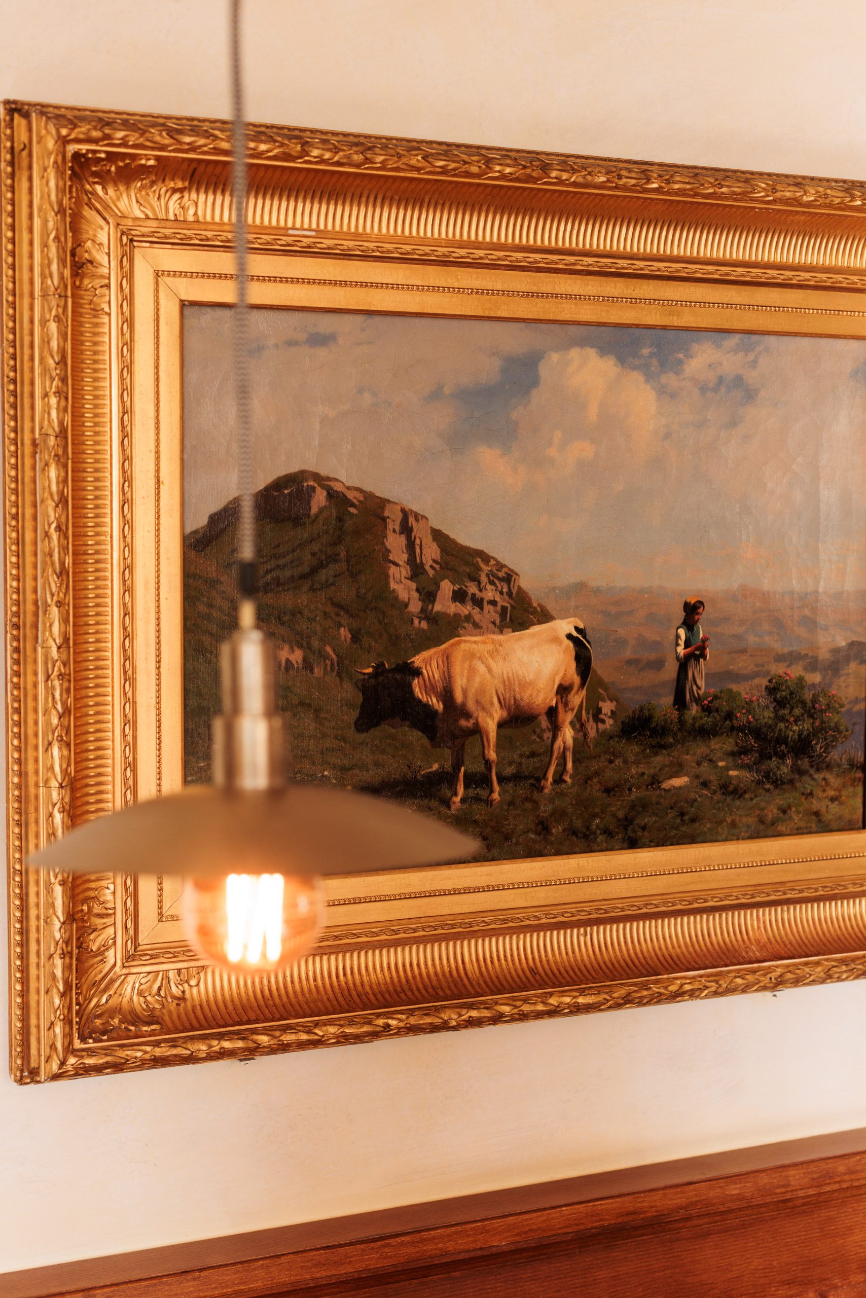 An der Wand der Gaststube des Hotels Sonne hängt ein gerahmtes Bild, das eine Kuh und zwei Menschen in einer grasbewachsenen Berglandschaft zeigt, im Vordergrund leuchtet eine Hängeleuchte.