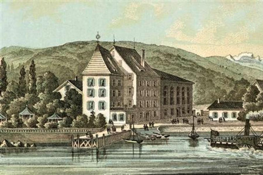 Eine historische Illustration des Historischen Hotels Sonne Küsnacht, eines großen Gebäudes am Wasser, umgeben von Bäumen und Hügeln, mit angedockten Booten und Spaziergängern am Ufer.