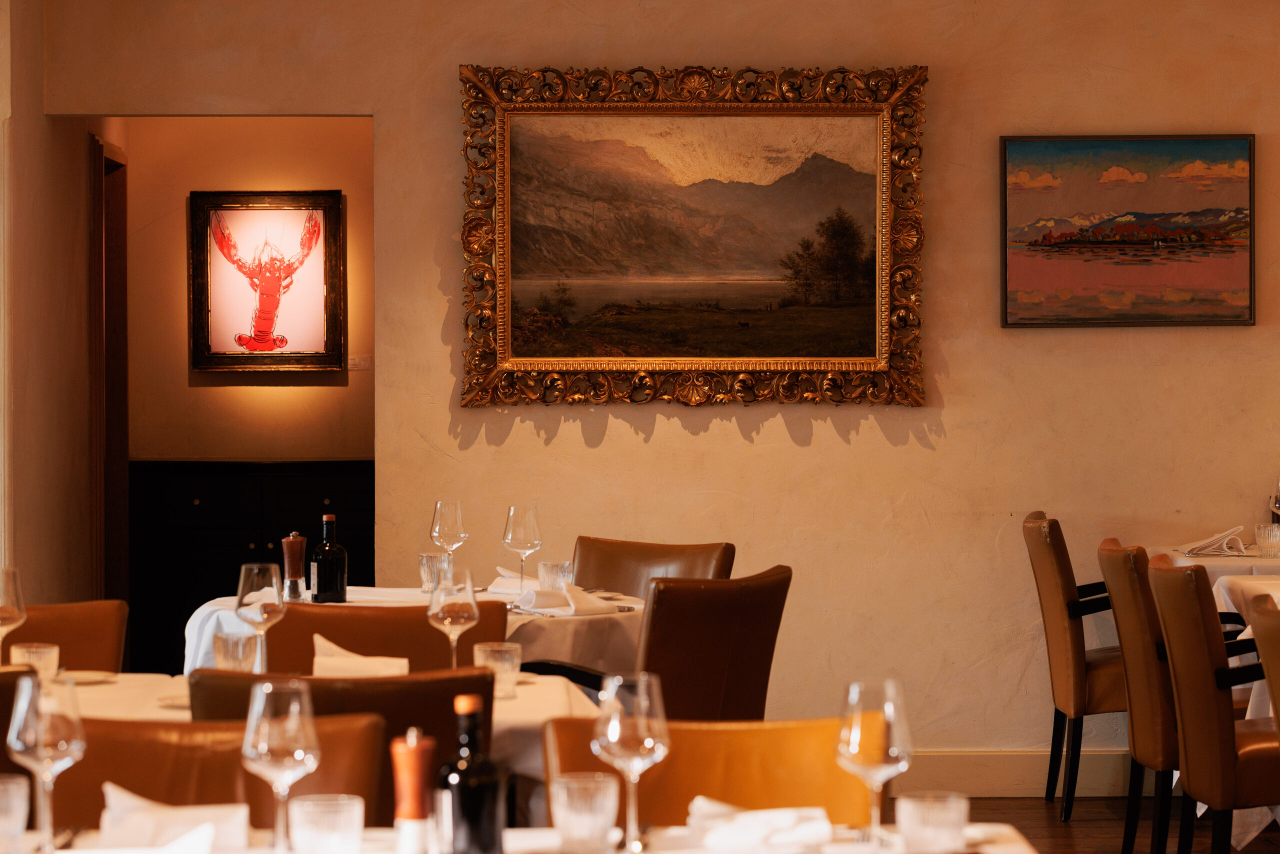 Elegantes Restaurantinterieur im Boutiquehotel Sonne in Küsnacht, mit ordentlich gedeckten Tischen, Weingläsern und braunen Stühlen. An den Wänden hängen gerahmte Kunstwerke, und die warme Beleuchtung schafft eine gemütliche Atmosphäre in der Nähe des Hotels am Zürichsee.