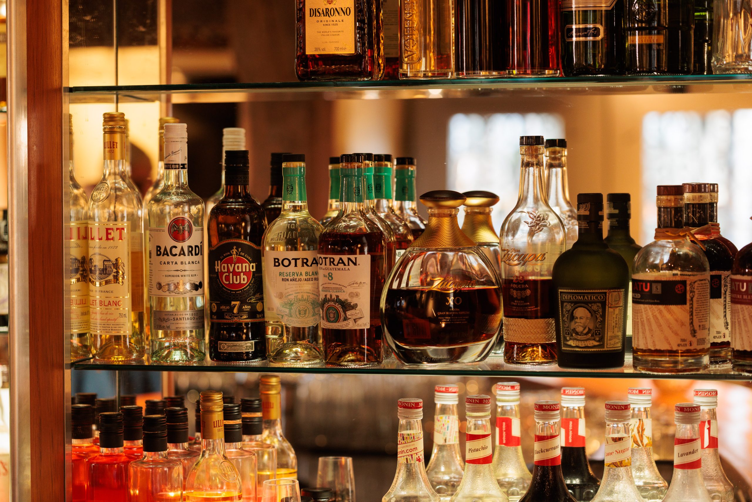 In der Hotel Bar Sonne stehen verschiedene Spirituosenflaschen, darunter Rum, Whisky und Liköre, in Glasregalen. Die Flaschen sind eng aneinandergereiht, und einige Etiketten sind deutlich sichtbar.