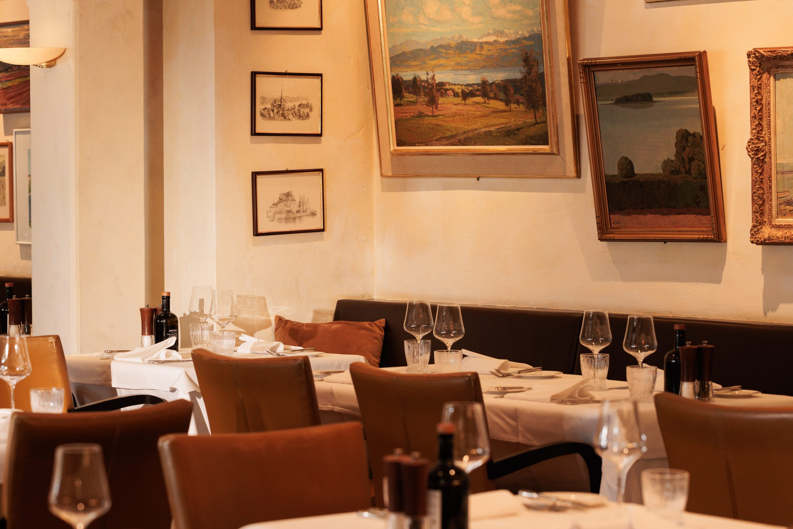 Elegantes Interieur des Restaurants Sonnengalerie mit ordentlich gedeckten Tischen, Weinflaschen und Gläsern. Gerahmte Bilder und Skizzen schmücken die Wände und schaffen eine warme Atmosphäre im Boutiquehotel Zürichsee. Es sind keine Menschen anwesend.