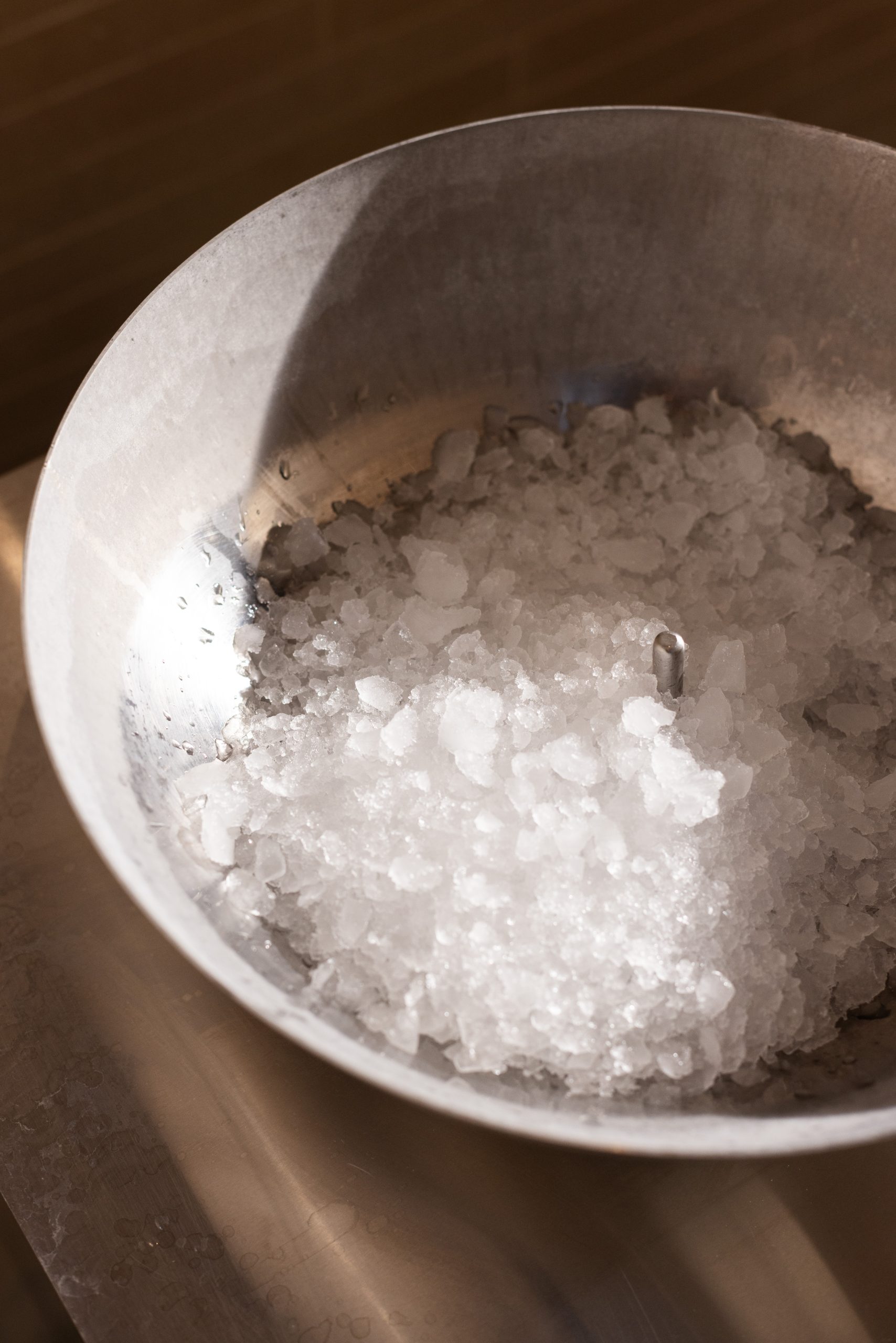 Eine Metallschale, gefüllt mit zerkleinertem Eis von Spa Sonne Küsnacht, steht auf einer Metallfläche, die teilweise vom Sonnenlicht beleuchtet wird.
