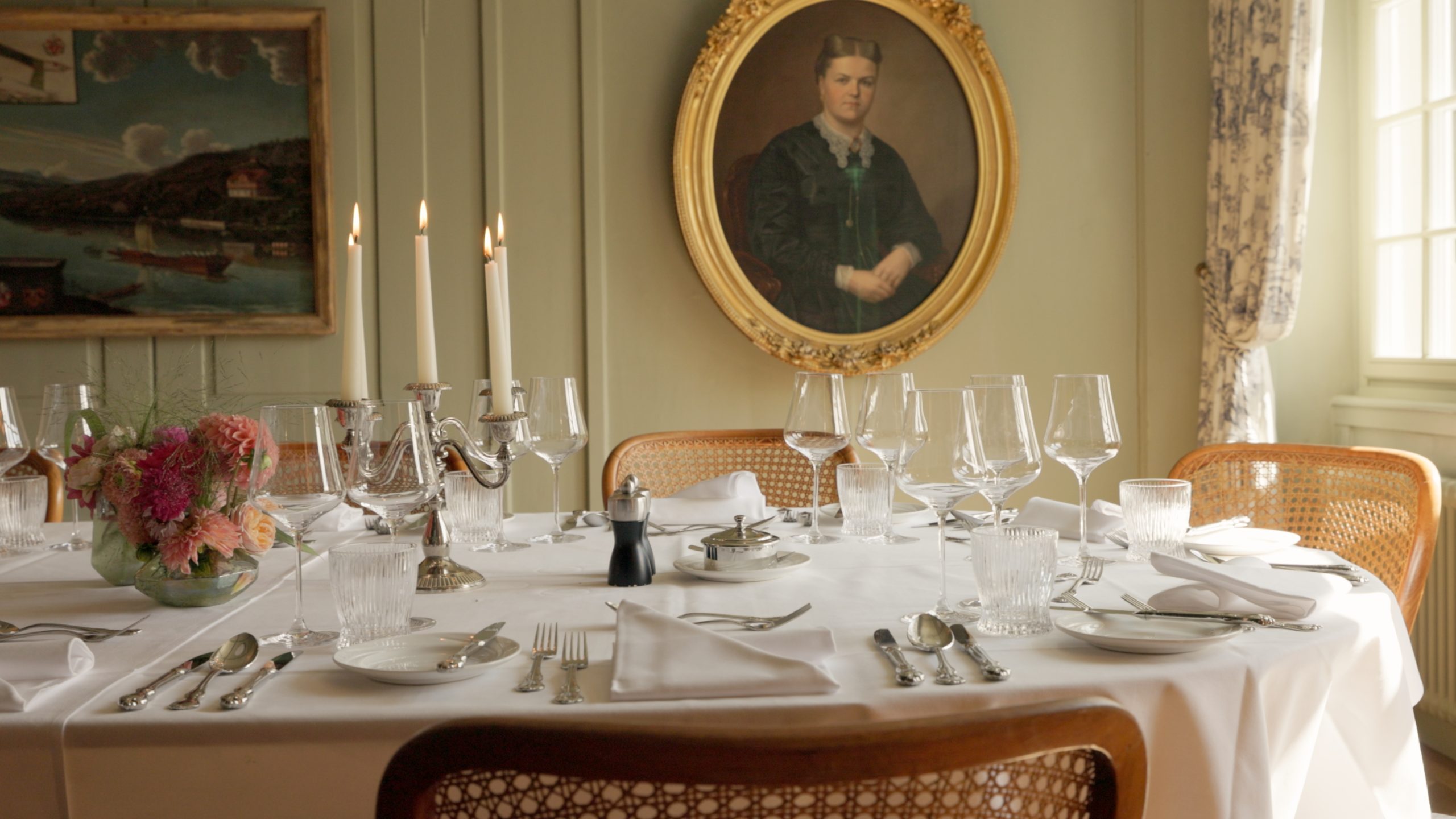 Ein formeller Esstisch mit Gläsern, Tellern und Silberbesteck auf einem weißen Tischtuch; in der Mitte ein silberner Leuchter und ein Blumenarrangement. Dahinter deutet ein goldgerahmtes Porträt auf die Eleganz des Boutiquehotels Sonne hin.